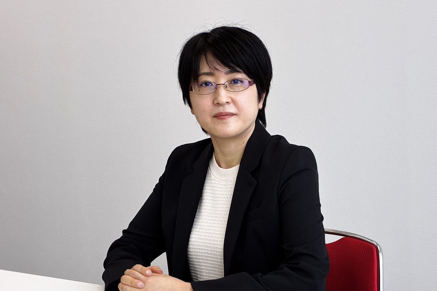机に手を組んでほほえむ石松 良子