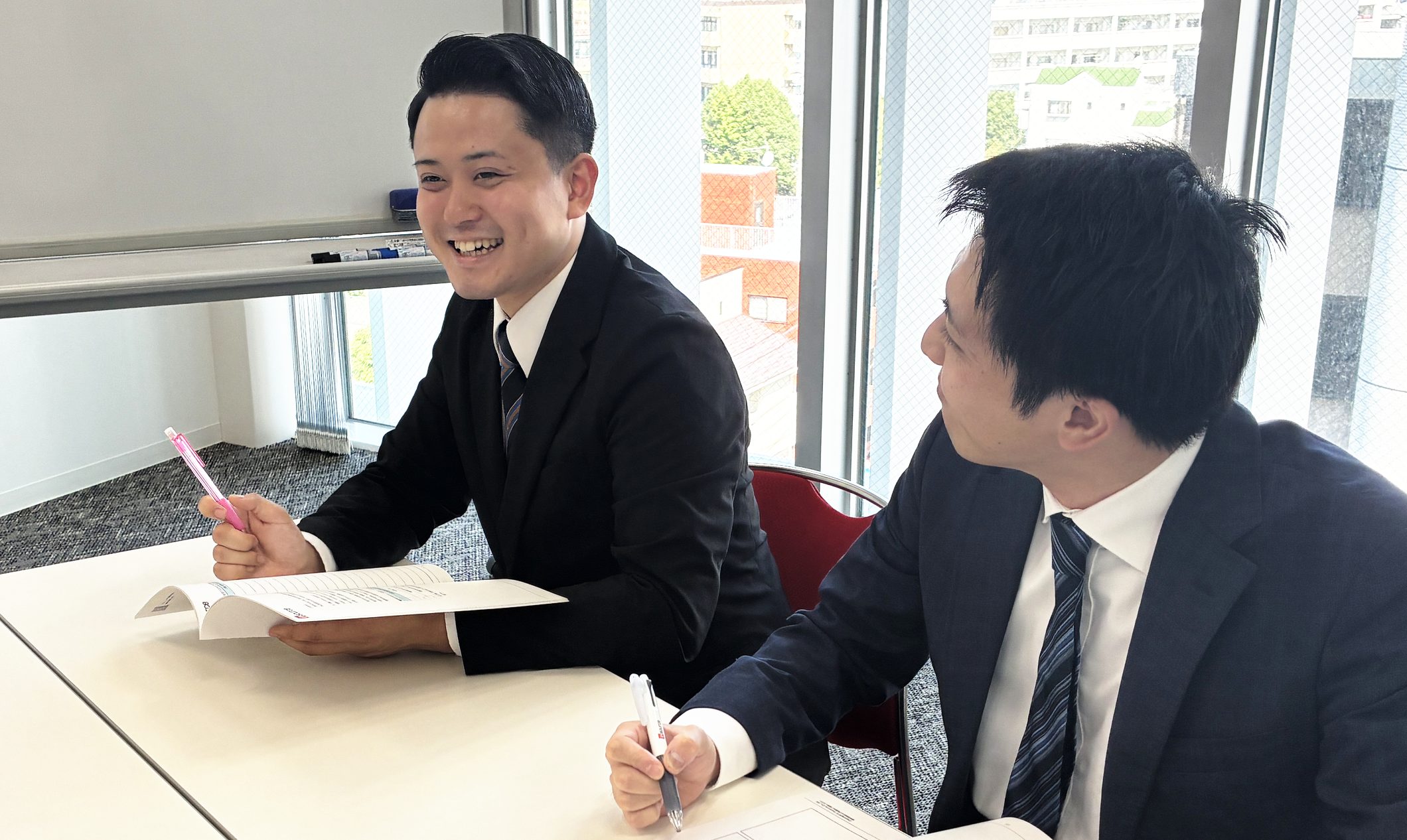 窓際の会議室で、資料を手に笑顔で話し合うICSのメンバー